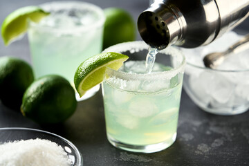 margarita cocktail is poured into a glass on a black background, selective focus.