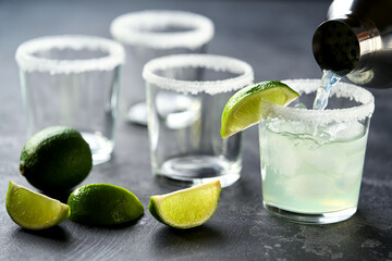 Bartender pours margarita cocktail in a glasses , selective focus on a black background.