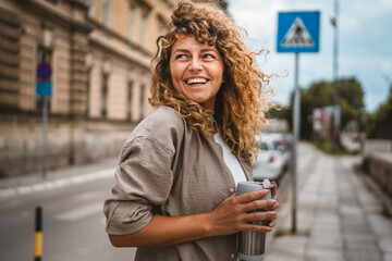 Fototapeta premium Adult beautiful woman stand on the street and hold thermos cup