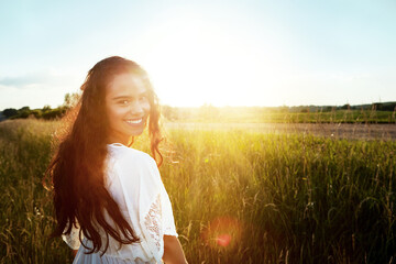 Fototapeta premium Portrait, woman and smile for travel in nature for summer adventure, explore outdoor or holiday. Lens flare, female person or space in field for trip, calm morning and vacation getaway in countryside