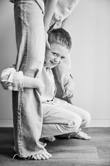 Young happy boy hugging mom's legs. Hyperactive kid holding his mother's legs. Clingy son wanting attention from mommy. Black and white image.