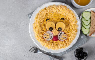 Fun food for kids breakfast - cute lion head made from scrambled eggs, cheese, radishes and black olives on white plate, Top view
