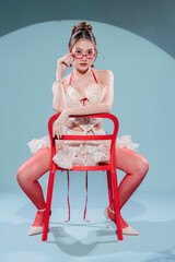 A stylish Asian fashion model poses in a studio wearing a chic coquette outfit with a cream lace corset, ruffled mini skirt, vibrant red tights, and cherry earrings for a trendy look.