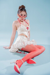A beautiful Asian fashion model celebrates her 30th birthday in a studio, wearing a cream corset, ruffled mini skirt, and bold red tights, posing with a cake for a trendy coquette aesthetic.