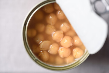 A close-up image of canned chickpeas in brine, half-open, against a gray fabric background