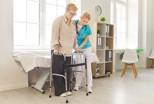Nurse helping elderly woman with walker during mobility rehabilitation session, physiotherapy in hospital. Senior patient standing and learning to walk with help and support of young caregiver