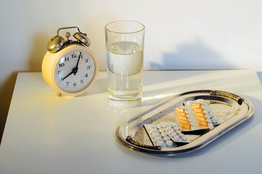 Alarm clock pills and water on bedside table at dawn in bedroom