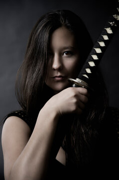 Portrait of woman holding katana sword in studio with dark background