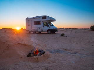 Off-grid camper van at sunset in the desert with a glowing campfire, symbolizing van life, freedom, outdoor living, slow travel, and a peaceful nomadic lifestyle.