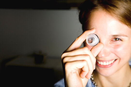 Smiling woman looking through glass bottle stopper indoors