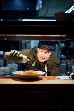 Chef plating gourmet dish in restaurant kitchen with focused expression