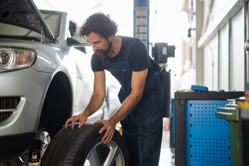 A skilled mechanic is focused on changing a tire in a car repair shop filled with tools and machinery in broad daylight, ensuring vehicle safety and performance.