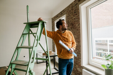 Proud owner planning renovation in new home by window and ladder