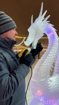 Artisan Sculptor Crafting Intricate Ice Dragon with Precision Tool Amidst Festive Atmosphere and Snowfall, Showcasing Skill and Creativity in Winter Fantasy