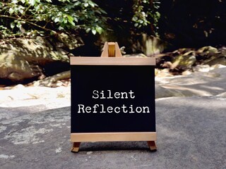 Chalkboard sign with words silent reflection placed outdoors, representing contemplation, mindfulness, simplicity, and thoughtful living concept.