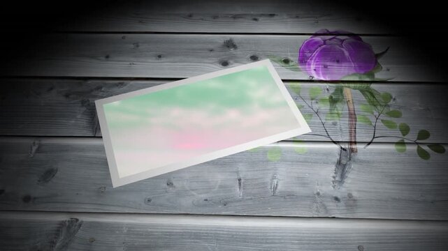Animation of frame with green image lying on wooden surface with flower