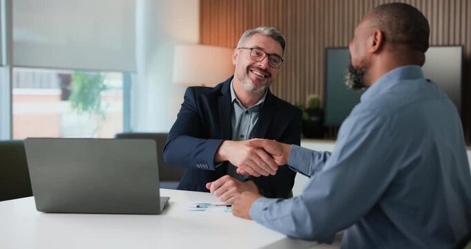 Happy, businessmen or meeting with handshake or laptop for corporate proposal or negotiation. Mature, business people or employees shaking hands for partnership, b2b deal or onboarding in workplace