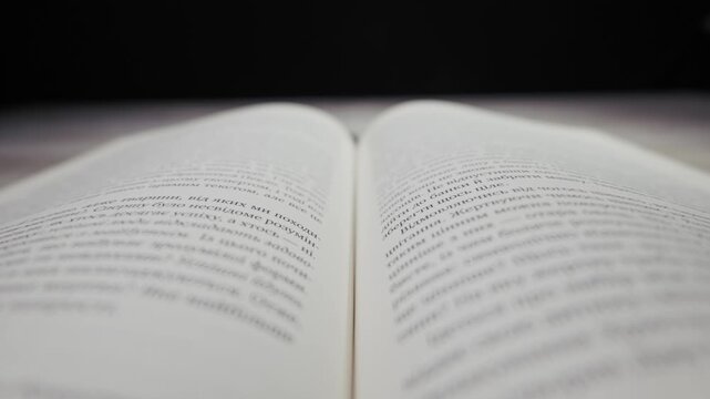 Camera focuses on the Cyrillic text of an open book lying on a table with a soft blurred background. Concept of wisdom, higher education, academic research, and literacy.