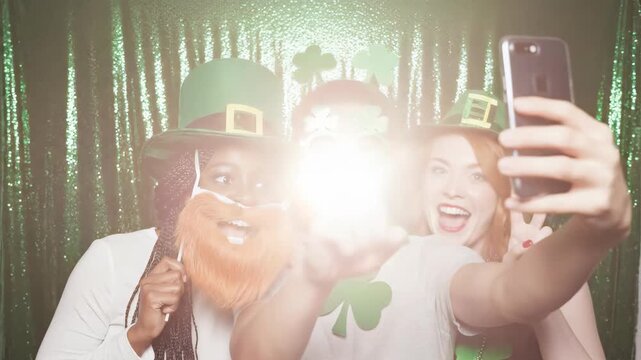 Diverse friends celebrating St. Patrick's Day with a selfie. Group of people in green costumes posing for a photo in front of a sequin backdrop. Festive holiday celebration concept