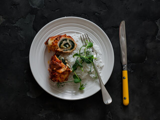 Chicken rolls stuffed with spinach, mozzarella and rice on a dark background, top view