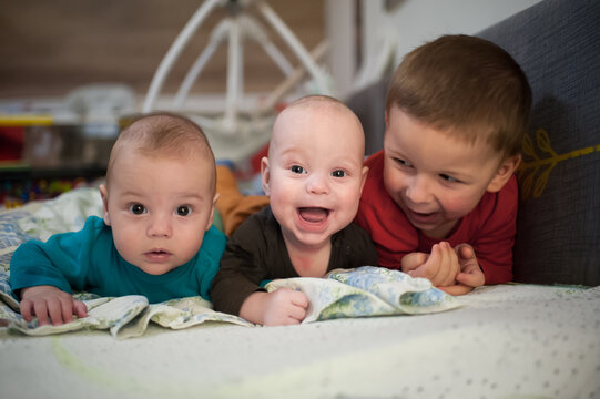 Three brothers are spending time together. An older brother smiles at his two baby twin brothers lying on their stomachs on a blanket during tummy time
