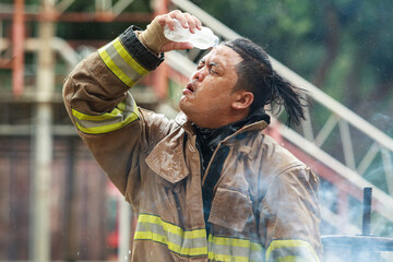 Exhausted Asian firefighter cooling down with water after emergency work