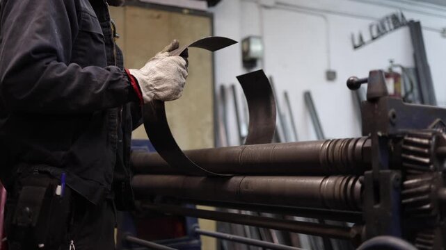 Metalworker shaping steel sheet using an industrial rolling machine in a factory, fabricating custom metal components with precision and craftsmanship in a workshop setting