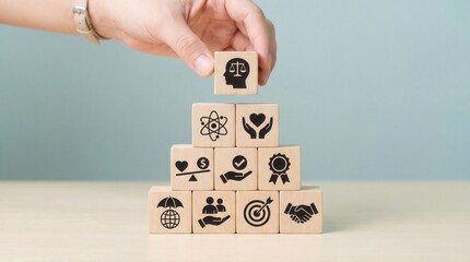 Human hand carefully places the final wooden cube symbolizing justice and ethics atop a pyramid of blocks representing important business and social values on a light blu