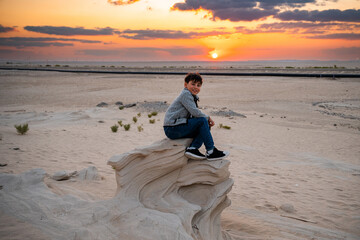 Boy sitting on al wathba fossil dunes at sunset
