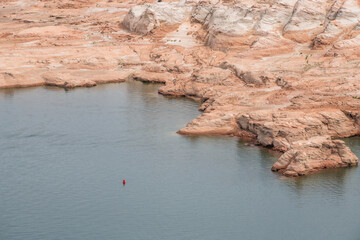 View of the arid landscape meets the tranquil waters of Lake Powell, with red marker afloat, a stark contrast in color, texture, and purpose, Page, Arizona, United States.