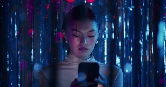 A woman uses a mobile phone with a serious look standing among sparkling blue tinsel