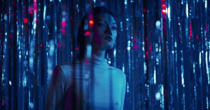 A serious young woman stands among the sparkling blue tinsel. She touches the tinsel with her hands