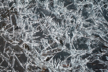 A detailed top-down view of sharp, crystalline ice structures formed on a dark water surface. The...