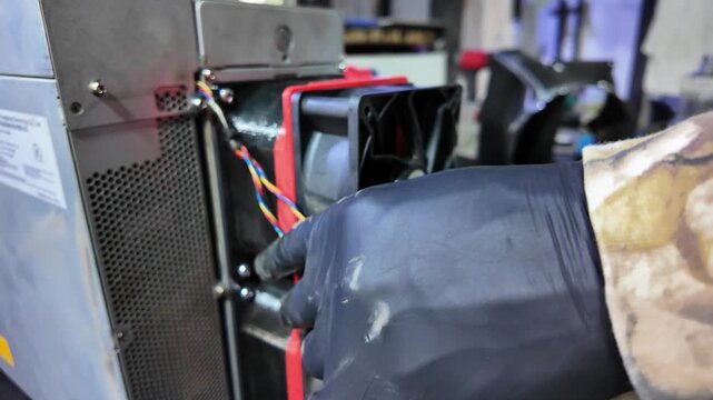 Close-up of a technician's hands in black gloves installing a powerful fan unit into a metal chassis for thermal management.