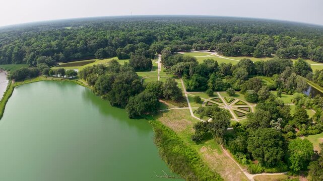 Drone footage captures a tranquil green pond with a formal cross-shaped walkway at Middleton Place Plantation near Charleston, SC, surrounded by lush trees and manicured lawns.