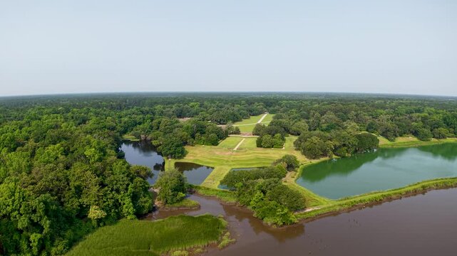 Aerial drone flies over cross-shaped islands and ponds at Middleton Place Plantation in Charleston, SC, showcasing symmetrical berms, grassy peninsulas, reflective water and surrounding woodland.