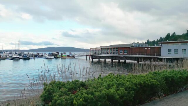 Drone footage of the Mill Bay Marina and waterfront buildings overlooking the Saanich Inlet, with moored sailboats, docks, and coastal forest in the Cowichan Valley region of Vancouver Island, British