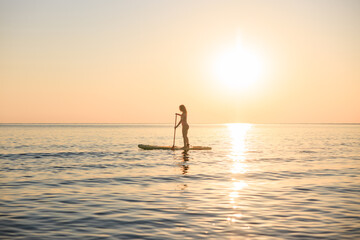 Fototapeta premium Young woman walking on stand up paddle sup boards by the sea during summer vacation