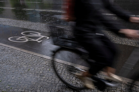 Urban street lane with cyclist on bicycle in rain showing wet asphalt motion during morning commute in city with blurred speed and reflections