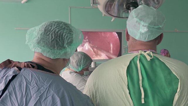 Team of surgeons looking at medical monitor screen performing laparoscopic surgery in hospital operating room