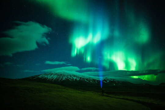 View of the vibrant aurora borealis dances above the snow-dusted mountains, casting an ethereal glow on the dark green fields below, Grundarfjordur, West Iceland, Iceland.