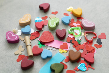 Colorful heart shapes collection with wooden beads, paper confetti, and love scroll on gray background. Festive variety for Valentine's Day DIY craft, romantic decoration, and wedding celebration.