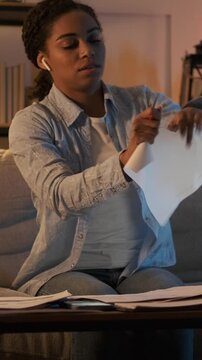 Vertical video of a frustrated young woman studying late at night, tearing up a paper, crumpling it, and then continuing to write with determination in her home.