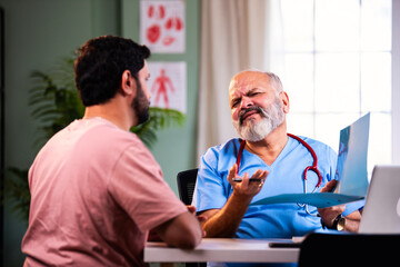 Fototapeta premium Senior Indian physician writes and explains medicine prescription to young male patient