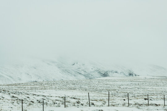 View of a snow-covered landscape under a flat, white sky, with a distant mountain range faded in the background, Hvitserkur, Vatnsnes peninsula, North Iceland, Iceland.