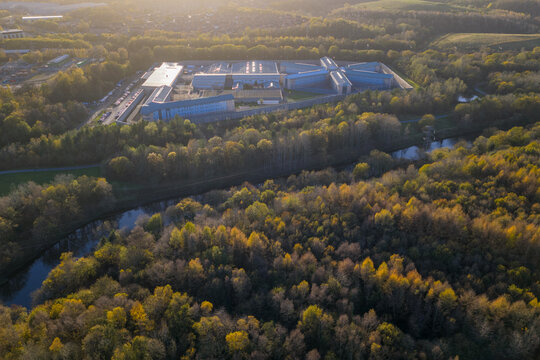 High-angle aerial shot of HMP Forest Bank in Salford, showing its radial architecture surrounded by autumn woodland and the River Irwell at sunset.