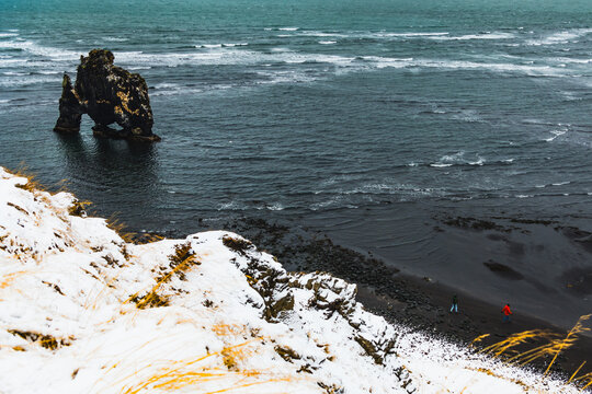 View of the imposing Hvitserkur sea stack rises from the dark ocean, a stark contrast to the snow-dusted black sand beach below, Blonduos, Vatnsnes peninsula, Iceland. - Powered by Adobe