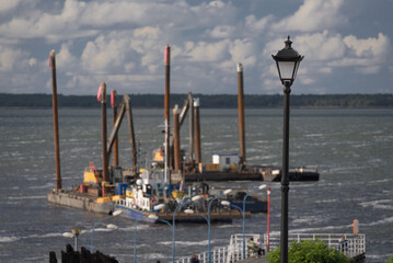 LANDSCAPE OVER SZCZECIN LAGOON - A stylish street lamp on the promenade, a pedestrian pier in Kamien Pomorski city and dredgers working on the water