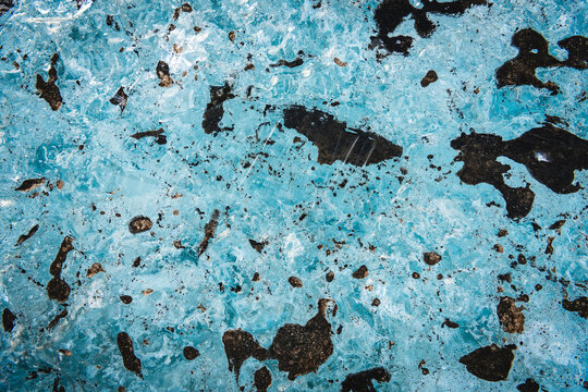 View of sapphire ice cave revealing a frozen world of translucent blue textures intermingling with dark, earthy deposits, Vatnajokull glacier, Iceland.