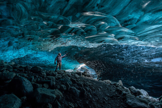 View of a lone figure stands in awe beneath the sapphire ice cave, where light dances on the frozen walls, creating a mesmerizing spectacle, Vatnajokull glacier, Iceland.